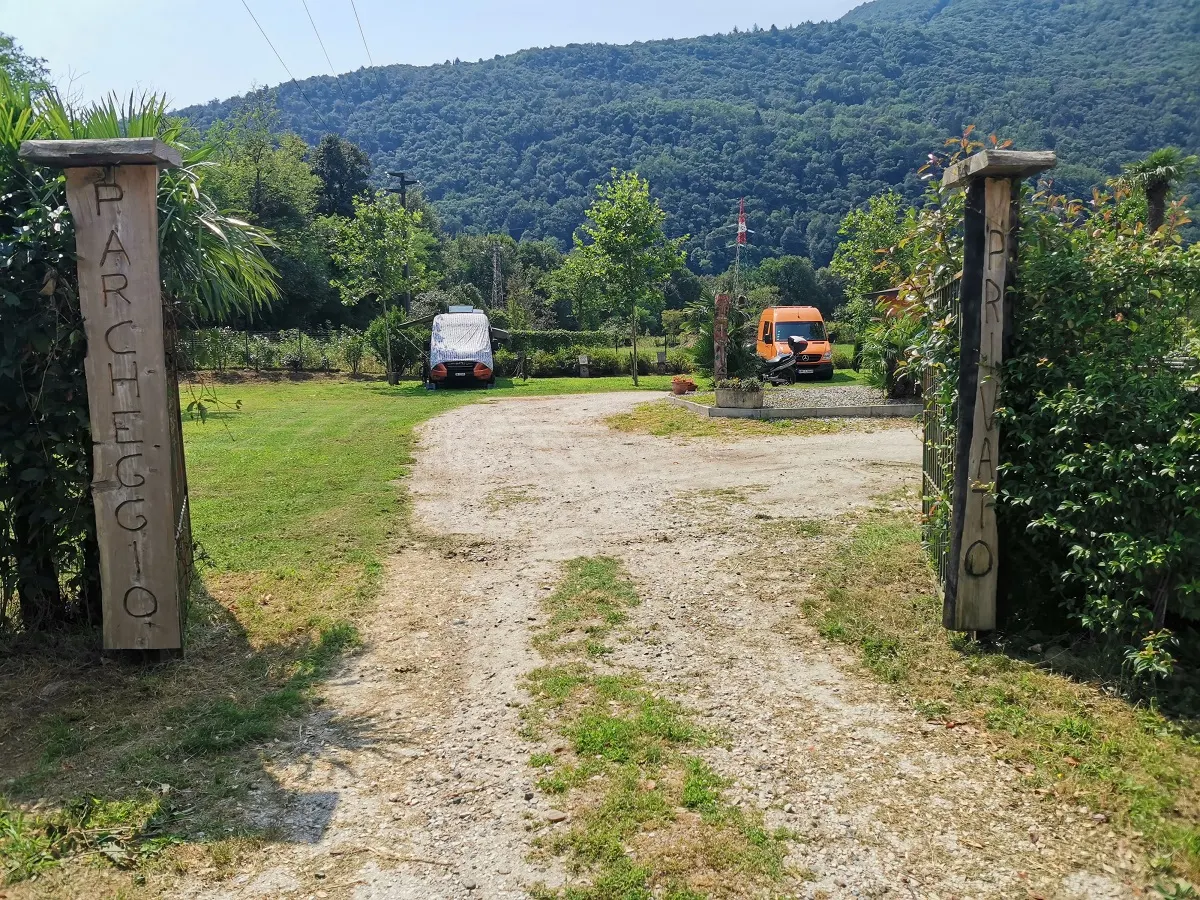 Die Zufahrt zwischen zwei geschnitzten Holzpfosten, dahinter Wiese und Berge