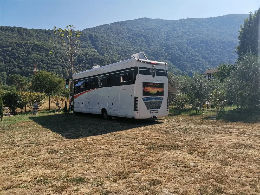 Ein großes Wohnmobil auf einem Grasstellplatz, im Hintergrund die Berge