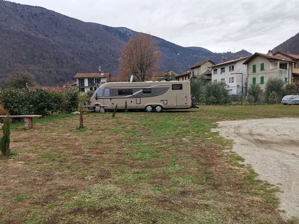 Ein zweiachsiges Wohnmobil im Winter, im Hintergrund der Ort und die Berge